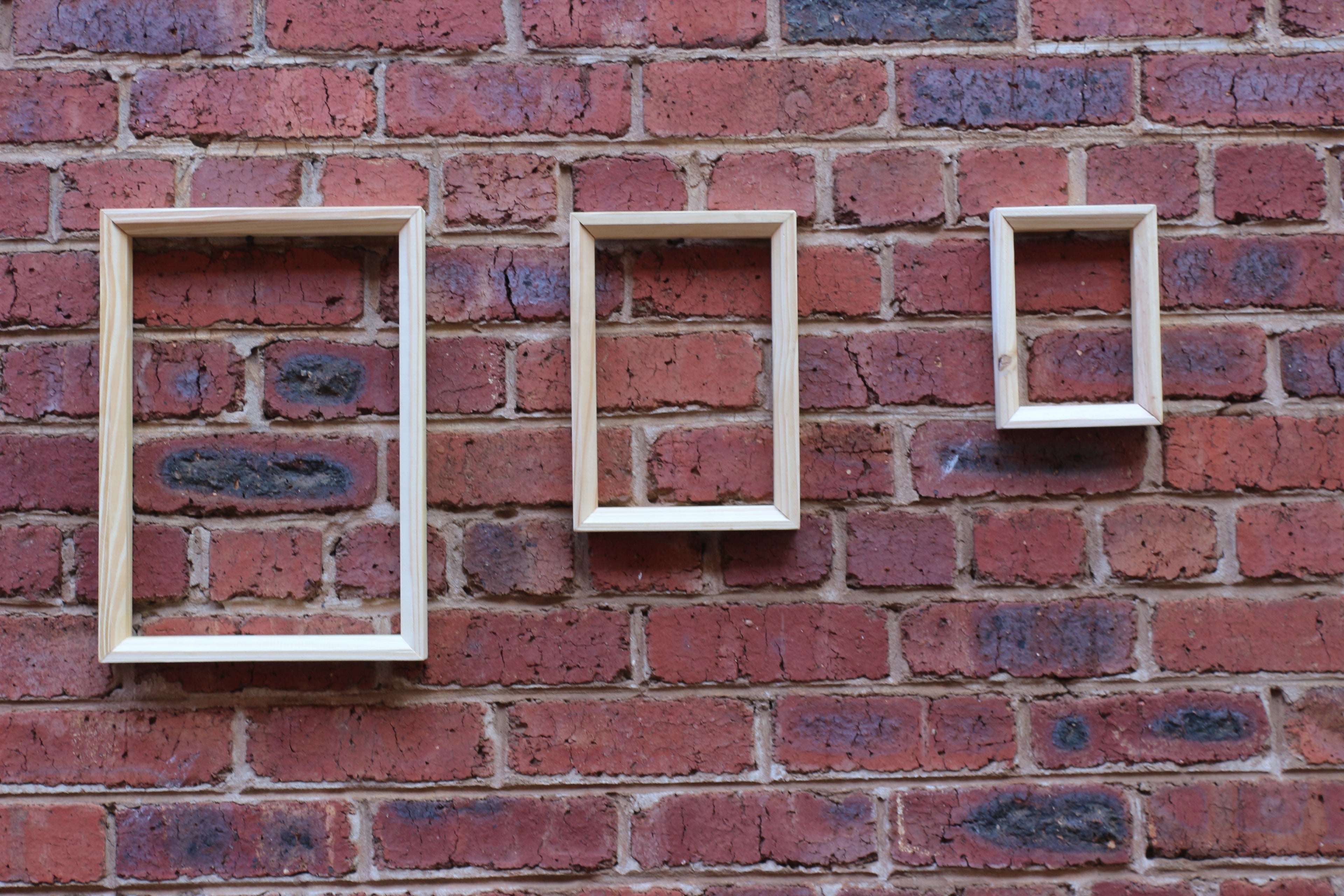 Three wooden picture frames of different sizes mounted on a brick wall.